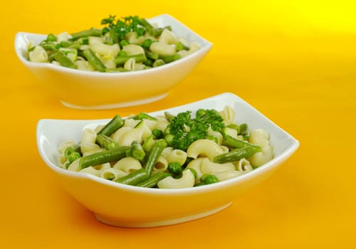 Pasta with peas, green beans, zucchini and spring onions and parsley on orange tablecloth (Selective Focus) 