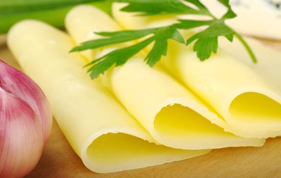 Slices of cheese on wooden plate with parsley and garlic