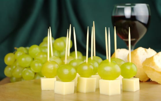 Cheese, grapes, baguette and red wine on a wooden board with green background (selective focus)