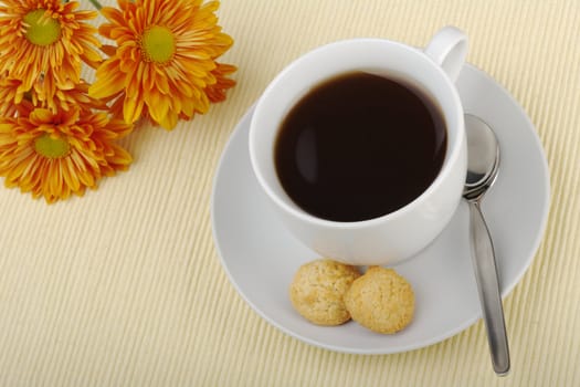 Blacktea in cup with saucer, teaspoon, biscuits and orange flower in the background on tablemat (Selective focus)