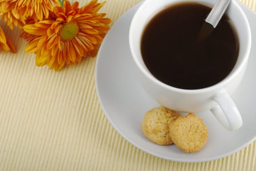 Blacktea in cup with saucer, teaspoon, biscuits and orange flower in the background on tablemat photographed from top (Selective Focus)