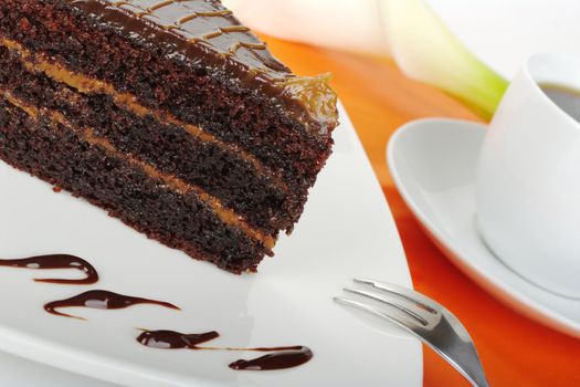 Chocolate cake on white with chocolate garnished plate, with coffee and a white arum lily in the background on orange (Selective Focus)