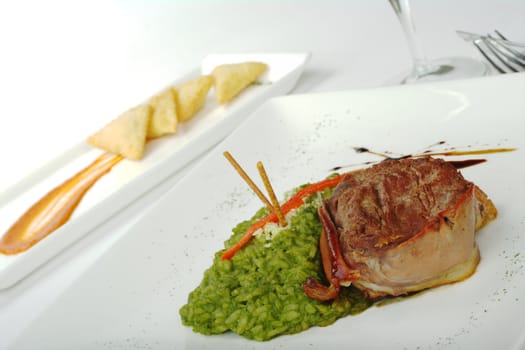 Beef meat wrapped in ham and rice mixed with spinach with empanada appetizer and a wine glass in the background (Selective Focus)