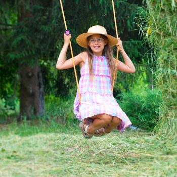 Young cute girl in the hat on swing in the garden