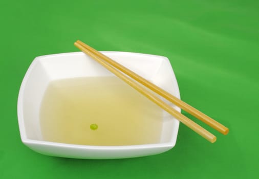Chinese diet: Vegetable broth with one pea and chopsticks on green (Selective Focus)