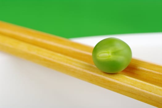 Pea on a pair of chopsticks on the rim of a white plate  (Selective Focus)