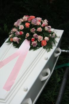A multicolored pink sympathy bouquet with pink ribbon on a white coffin