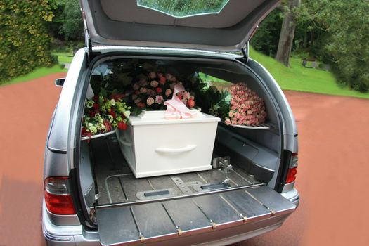 A white coffin, covered with flowers in a grey hearse