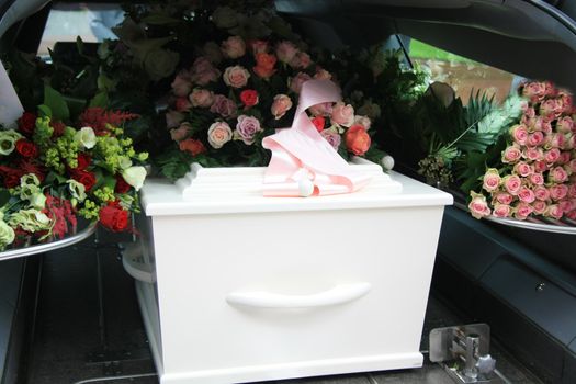 A white coffin, covered with flowers in a grey hearse