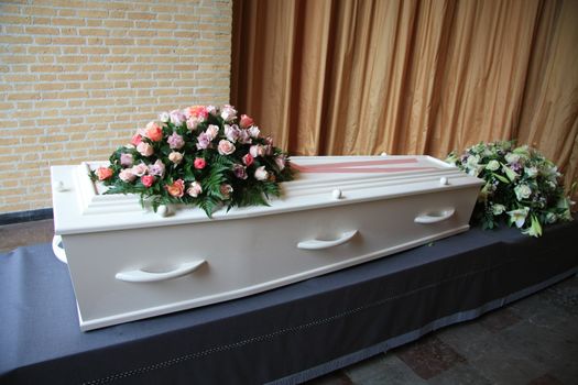A whtie coffin with pink flowers at a funeral service