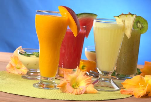 Mango, pineapple, watermelon and kiwi smoothies surrounded by gladiolus flower (Selective Focus, Focus on the mango and pineapple smoothies in the front)