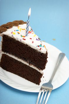 A slice of chocolate cake with a single lit candle.