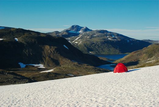 Camping with a red tent on a snowfield with a view on mountains and lakes along the Nordkalottleden, Scandinavia 