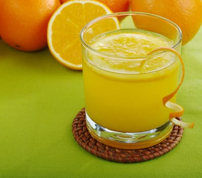 Fresh orange juice with orange slice in glass and oranges in background on green table mat (Selective Focus)