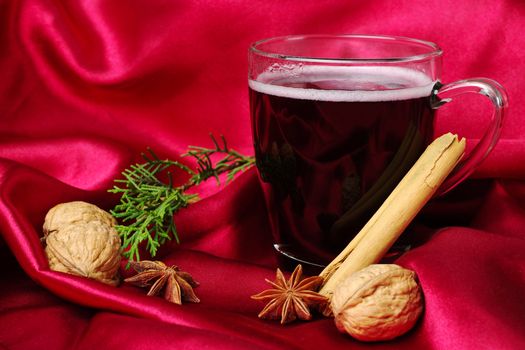 Hot spiced red wine with cinnamon, star anise, walnuts and a branch of evergreen with red background (Selective Focus)