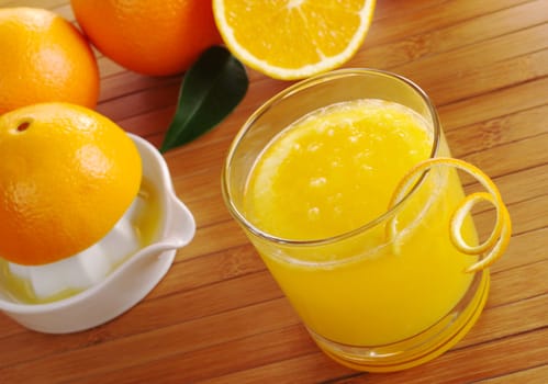 Fresh orange juice with orange slice in glass with squeezer and oranges in background on table mat (Selective Focus)