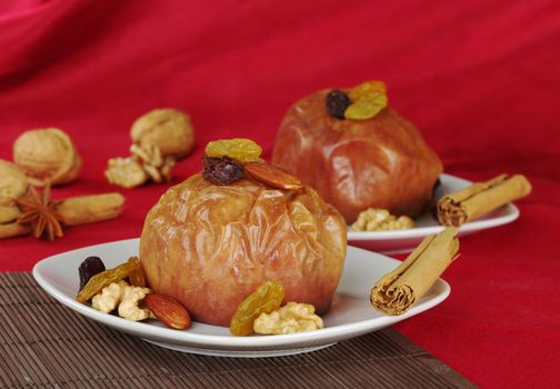 Baked apple with walnuts, raisins, almonds and cinnamon on brown table mat and red fabric as background (Selective Focus) 