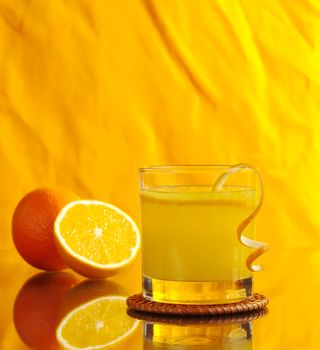 Fresh orange juice in glass with orange peel and oranges on orange background (Selective Focus) 