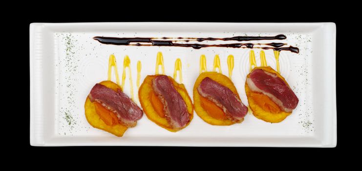 Appetizer: Duck meat with sweet potato puree on sweet potato chip on white rectangular plate isolated on black 