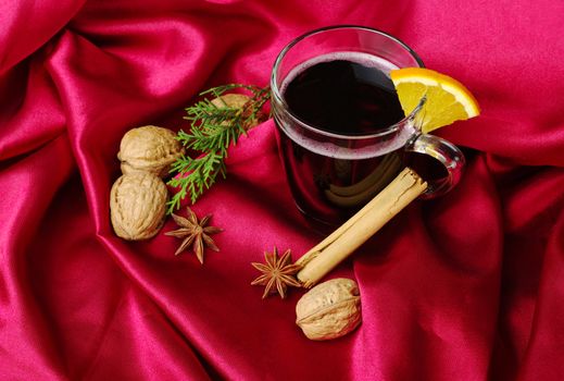 Hot spiced red wine with orange, cinnamon, star anise, walnuts and a branch of evergreen on red fabric (Selective Focus)