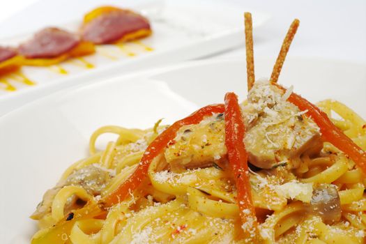 Fettuccine with chicken, mushrooms, red bell pepper with ham on camote appetizer in the background (Selective Focus)