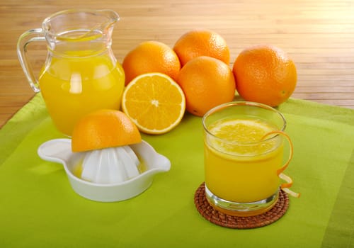 Fresh orange juice with orange juice squeezer and oranges on green and a wooden mat (Selective Focus)