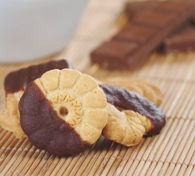 Butter cookies dipped in milk chocolate icing with chocolate bar and bowl in the background (Selective Focus)  