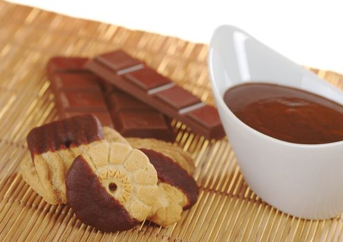 Butter cookies dipped in milk chocolate icing with chocolate dip in white bowl and chocolate bar on table mat (Selective Focus)  