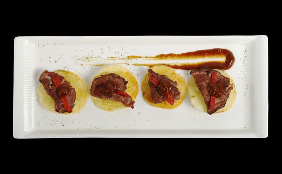 An appetizer of meat on potato chips with ketchup, photographed from above and isolated on black