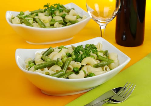 Pasta with peas, green beans, zucchini and spring onions and parsley served with red wine on orange tablecloth (Selective Focus, Focus on front plate) 