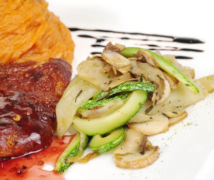 A pile of fried vegetables (zucchini, mushroom) with a piece of meat and mashed sweet potatoes in the background (Selective Focus, Focus on the pile of vegetables)