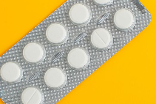 Close-up of a pack of white pills on yellow background.