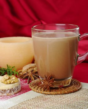 Hot chocolate in glass cup with anise, cookie, and candle in the background (Selective Focus, Focus on the glass cup)