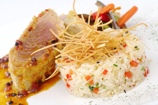 Vegetable risotto with fried thin potatosticks on top, and fish with vegetables in the background (Selective Focus, Focus on the front of the rice)