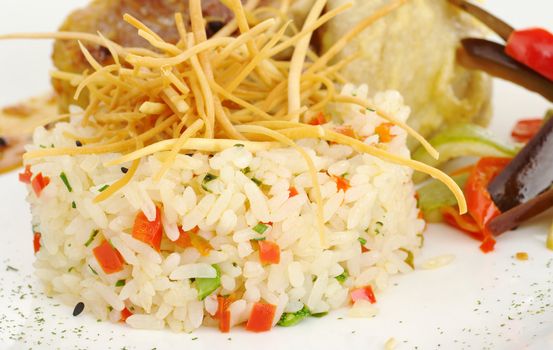 Vegetable risotto with fried thin potatosticks on top, and fish with vegetables in the background (Selective Focus, Focus on the front of the rice)