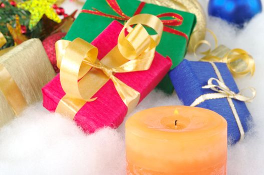 Lit orange candle and colorful presents with Christmas decoration on cotton (Selective Focus, Focus on candle)