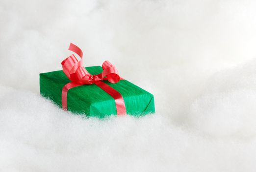 Green Christmas gift with red ribbon on white cotton that looks like clouds (Selective Focus, Focus on the first half of the gift box)