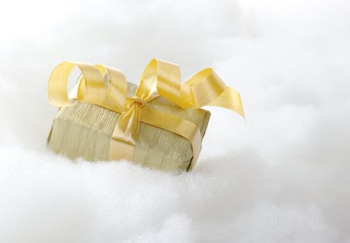 Golden Christmas gift with ribbon on white cotton that looks like clouds (Selective Focus, Focus on the front of the gift box)