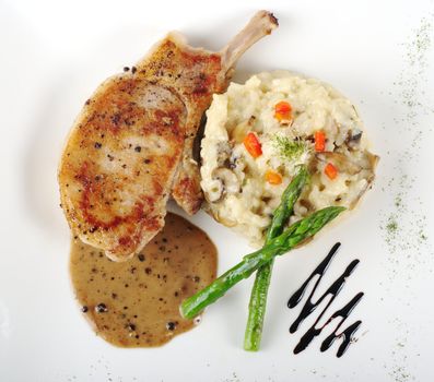 Risotto, green asparagus and meat with gravy on a garnished white plate photographed from above 