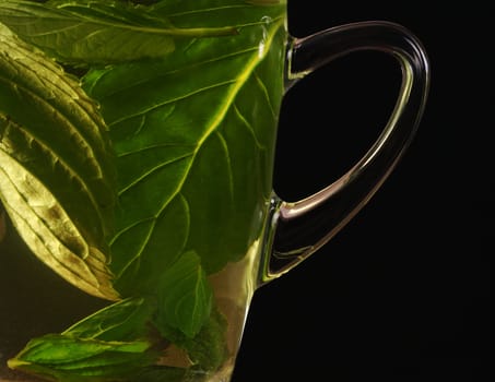 Fresh mint tea out of mint leaves in a glass cup photographed on black (Selective Focus, Focus on the handle of the glass) 