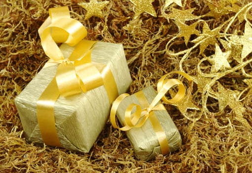 Boxes wrapped in golden paper with golden ribbon on brown moss with golden stars in the background (Selective Focus, Focus on front)