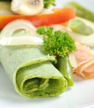 Rolled thin green colored pancake (colored with spinach in dough) with vegetables on top (Selective Focus, Focus on the front of the pancake) 