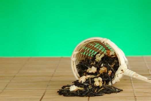 Green jasmine tea in wooden tea strainer on wooden table mat with green background (Selective Focus, Focus on the front of the tea leaves)  