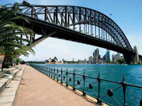 Walking on the path that leads beneath the Sydney Harbour Bridge in Australia.  Cityscape of Sydney behind.
