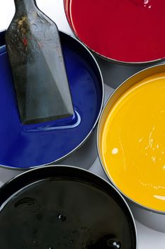 Tubs of printing press inks, cyan, magenta, yellow and black.  An ink knife rests in the cyan container.
