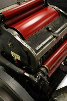 Image of an old windmill printing press / die cutter / numbering machine, with bright red ink on it's rollers.
