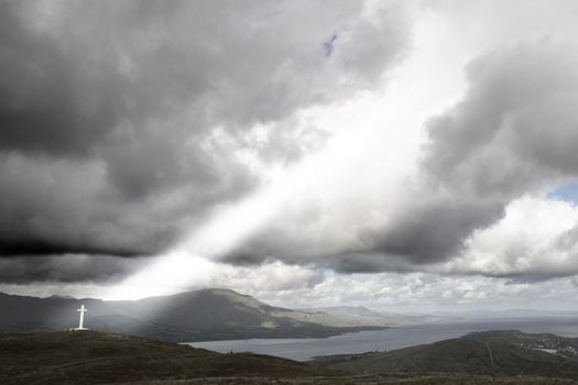 concrete Cross on top of bear island in county Cork Ireland with gods light shinning down