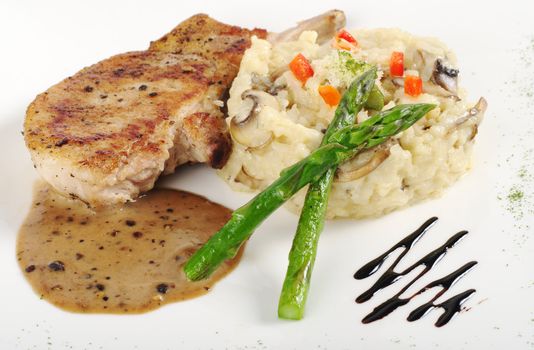 Risotto, green asparagus and meat with gravy on a garnished white plate (Selective Focus, Focus on the head of the asparagus, part of the meat and the rice)