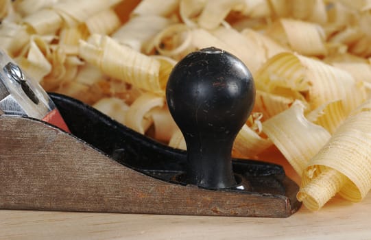 Black metal wood planer and shavings on wooden plank (Selective Focus, Focus on the handle and the front of the planer and the shaving in the front)