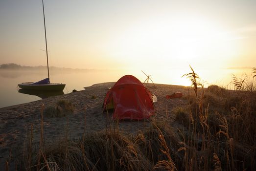 Red tent and small sailing boat on sandy shore in a cold morning 